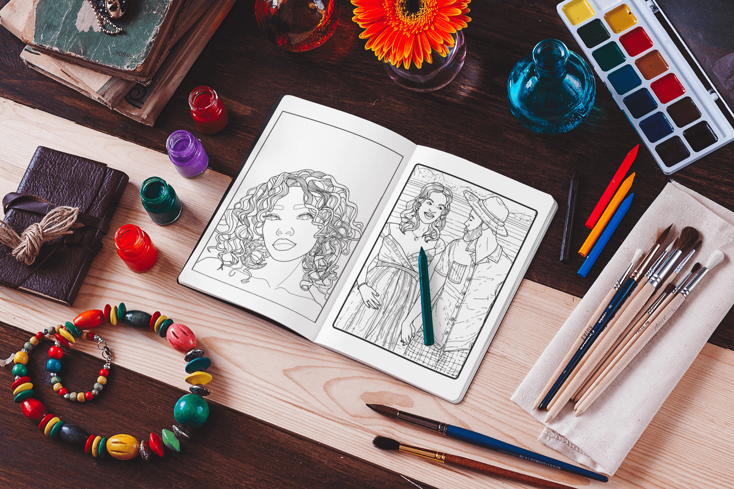 Coloring book open to Afro-American women's portraits, surrounded by art supplies and creativity tools.