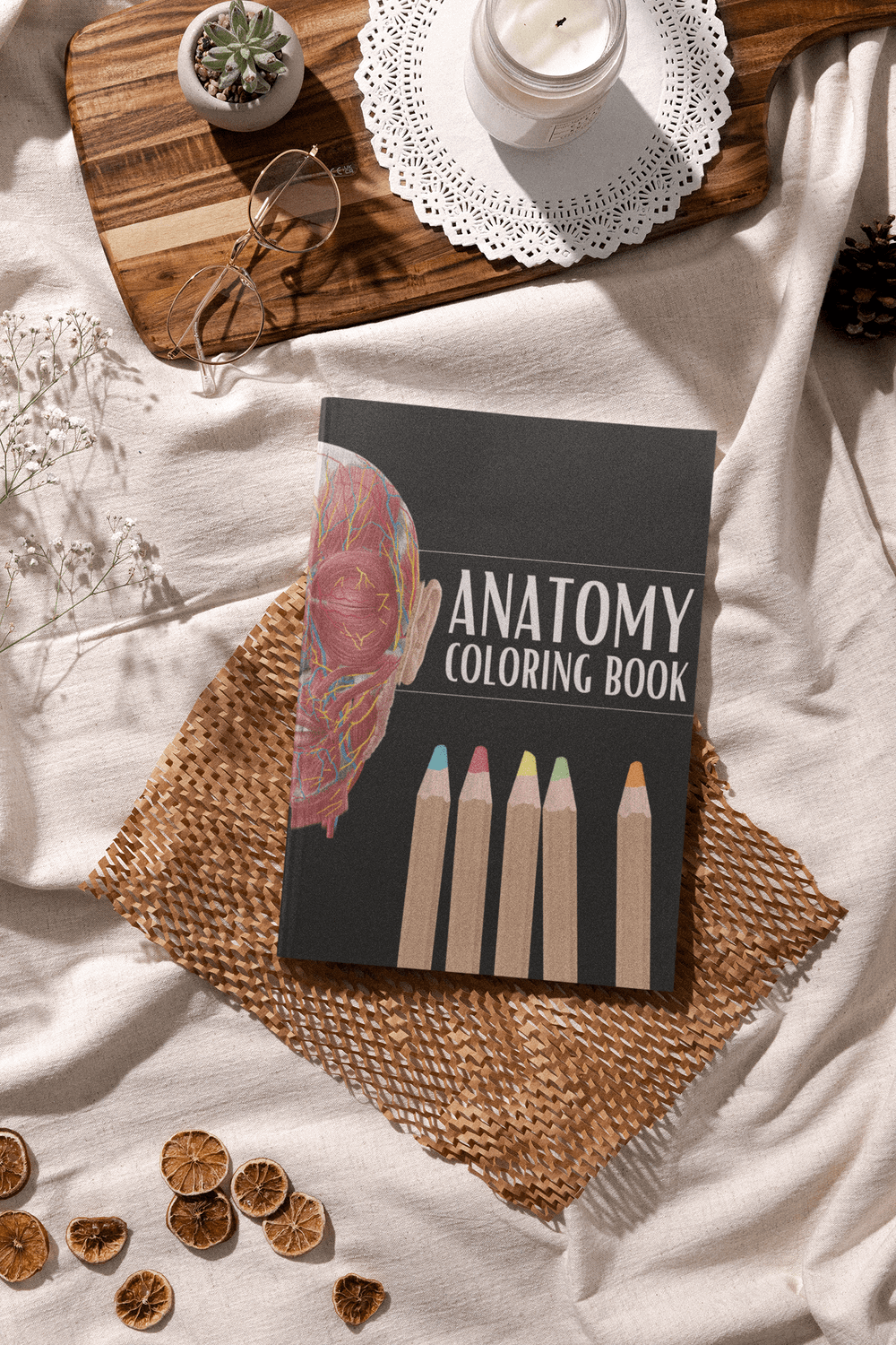 Anatomy Coloring Book on a textured fabric, featuring colored pencils and decorative elements.