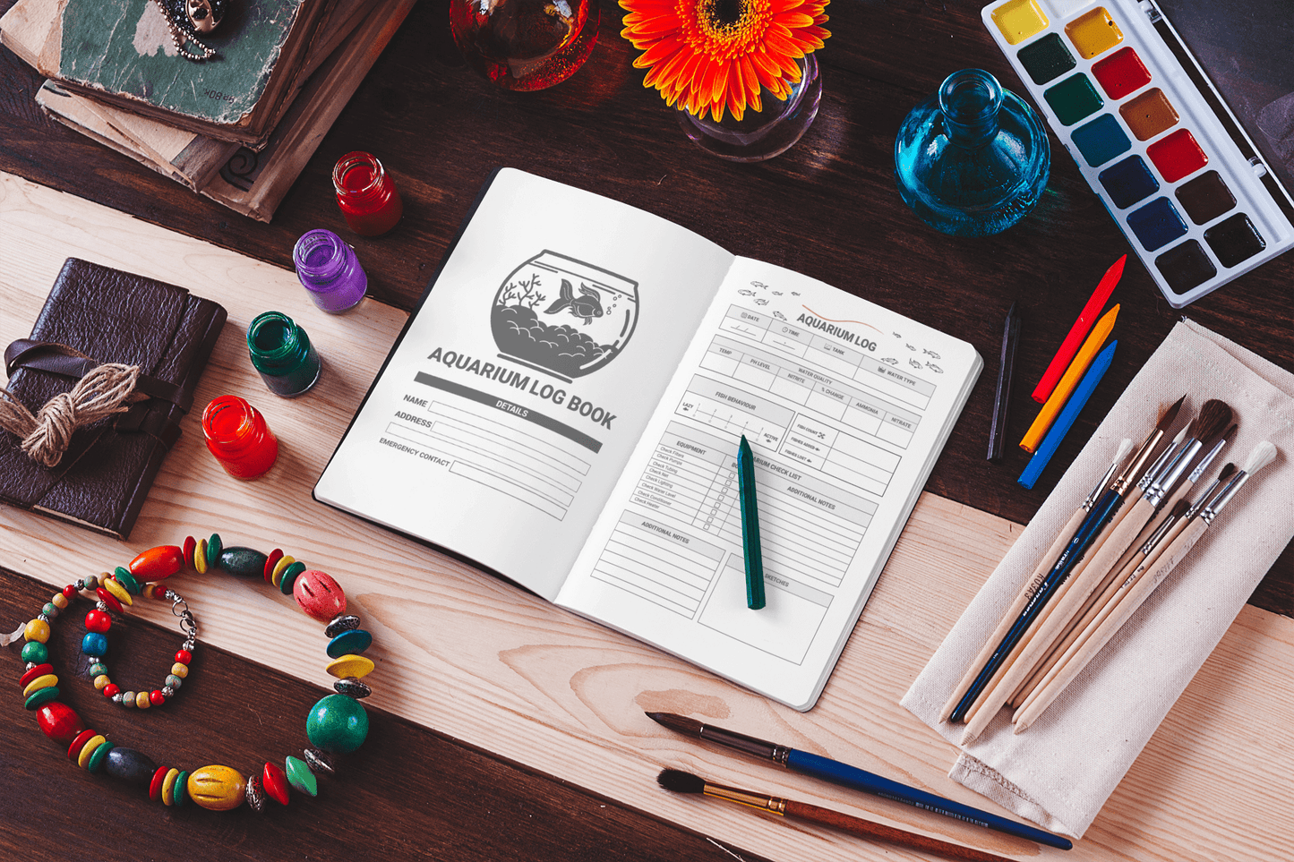 Aquarium log book open on a table surrounded by paint supplies, brushes, and accessories for aquarium maintenance.