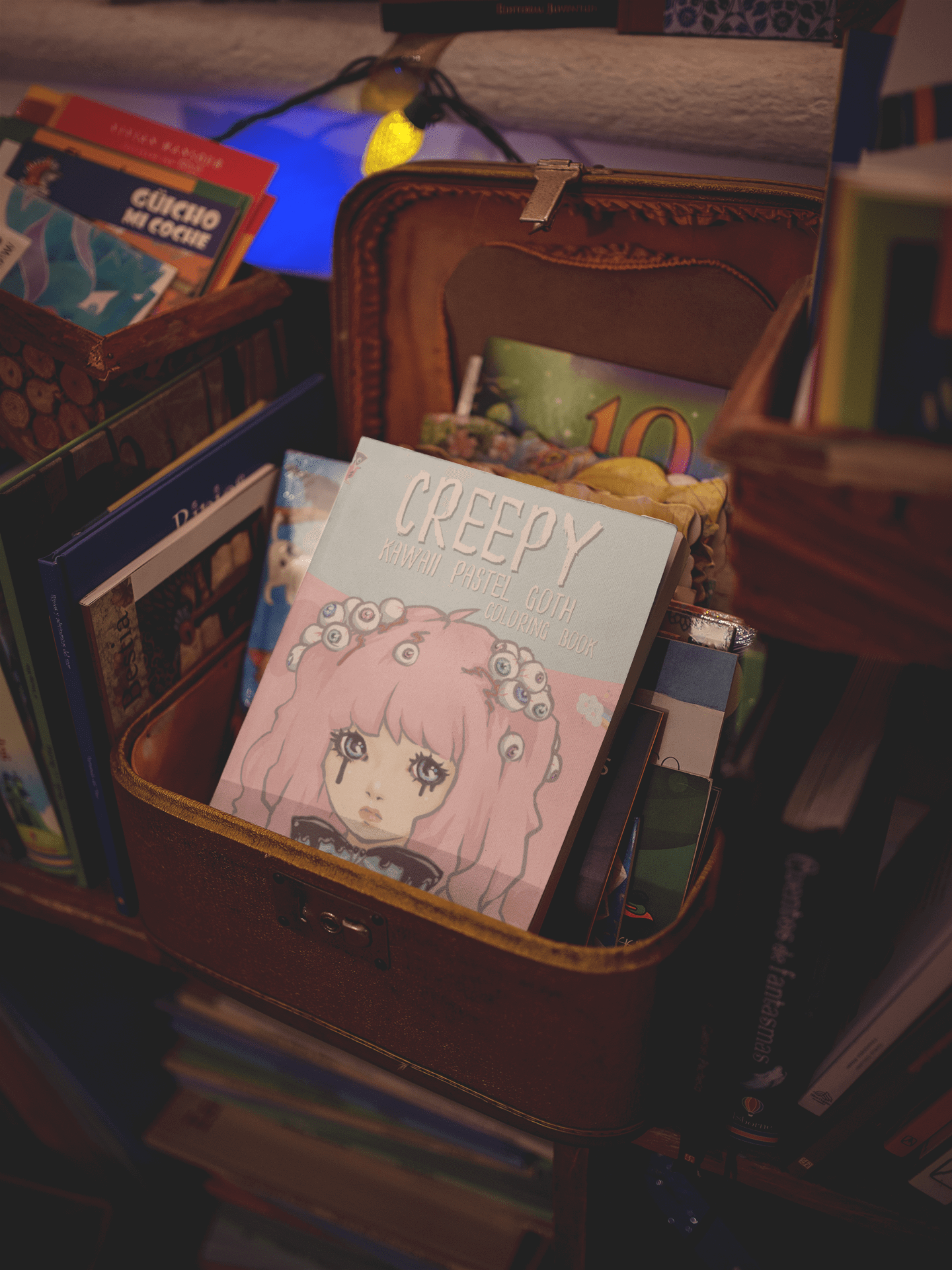 Creepy Kawaii Pastel Goth coloring book displayed in a cozy bookshelf with various books around it.