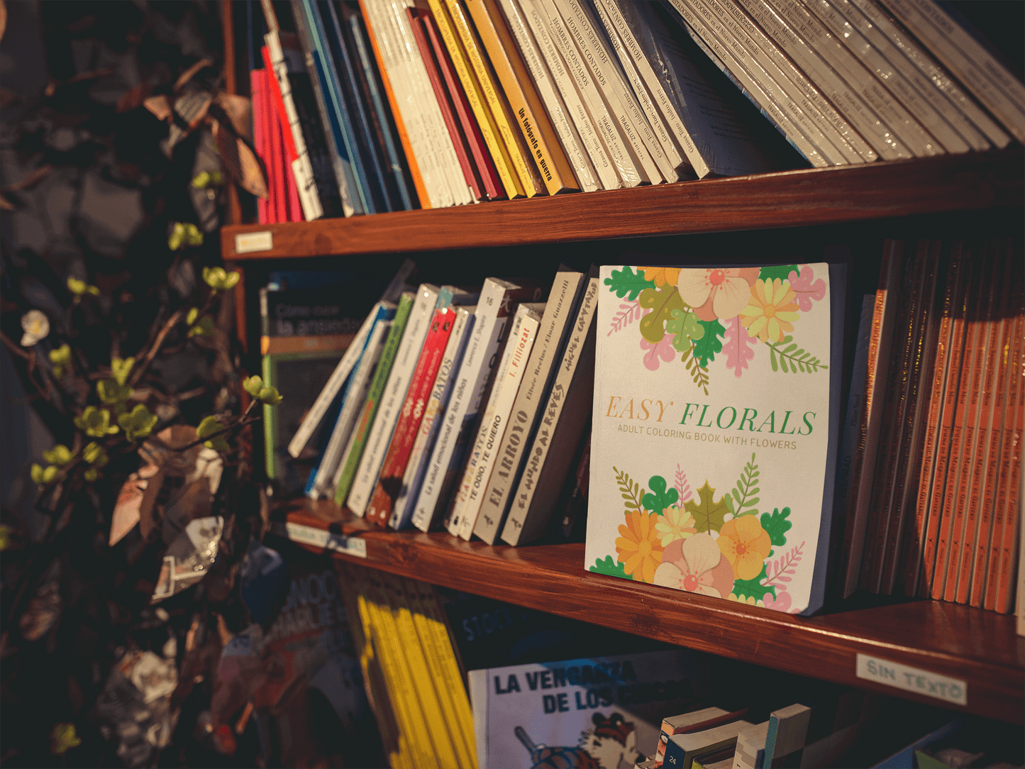 Easy Florals adult coloring book displayed on a wooden shelf surrounded by other colorful books.
