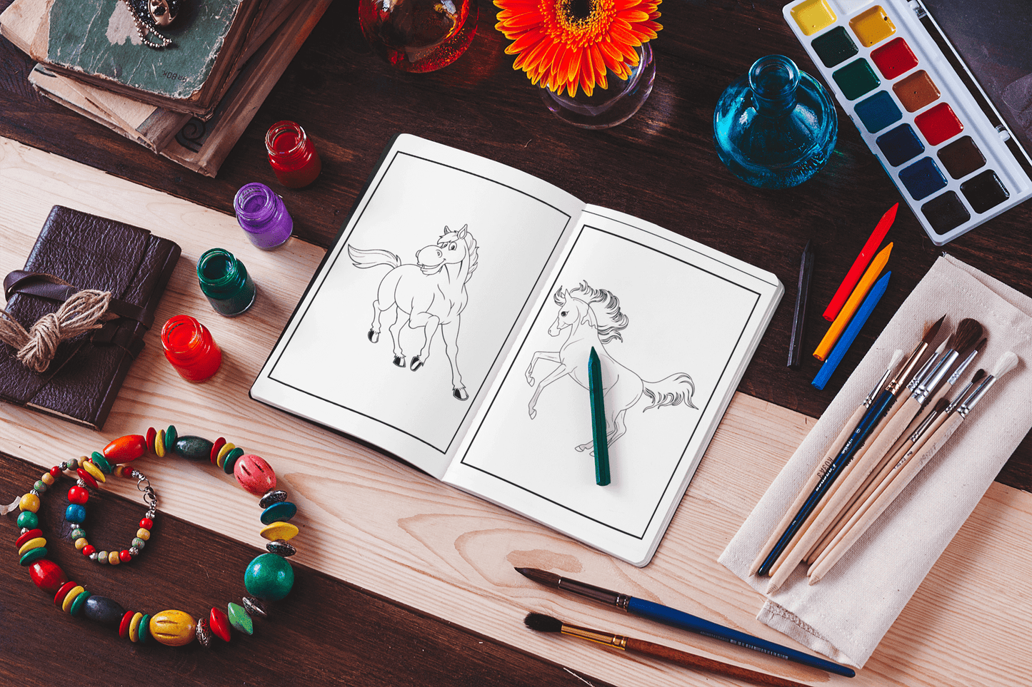 Open coloring book with horse illustrations, surrounded by art supplies and colorful beads on a wooden table.