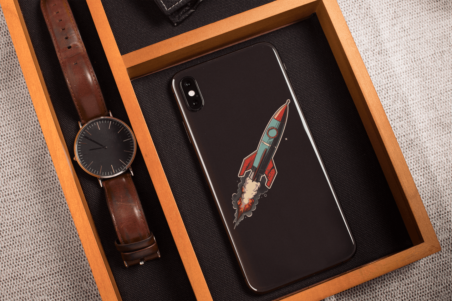 Atomic Age spacecraft sticker design on a phone, resting in a wooden tray with a watch and accessories.