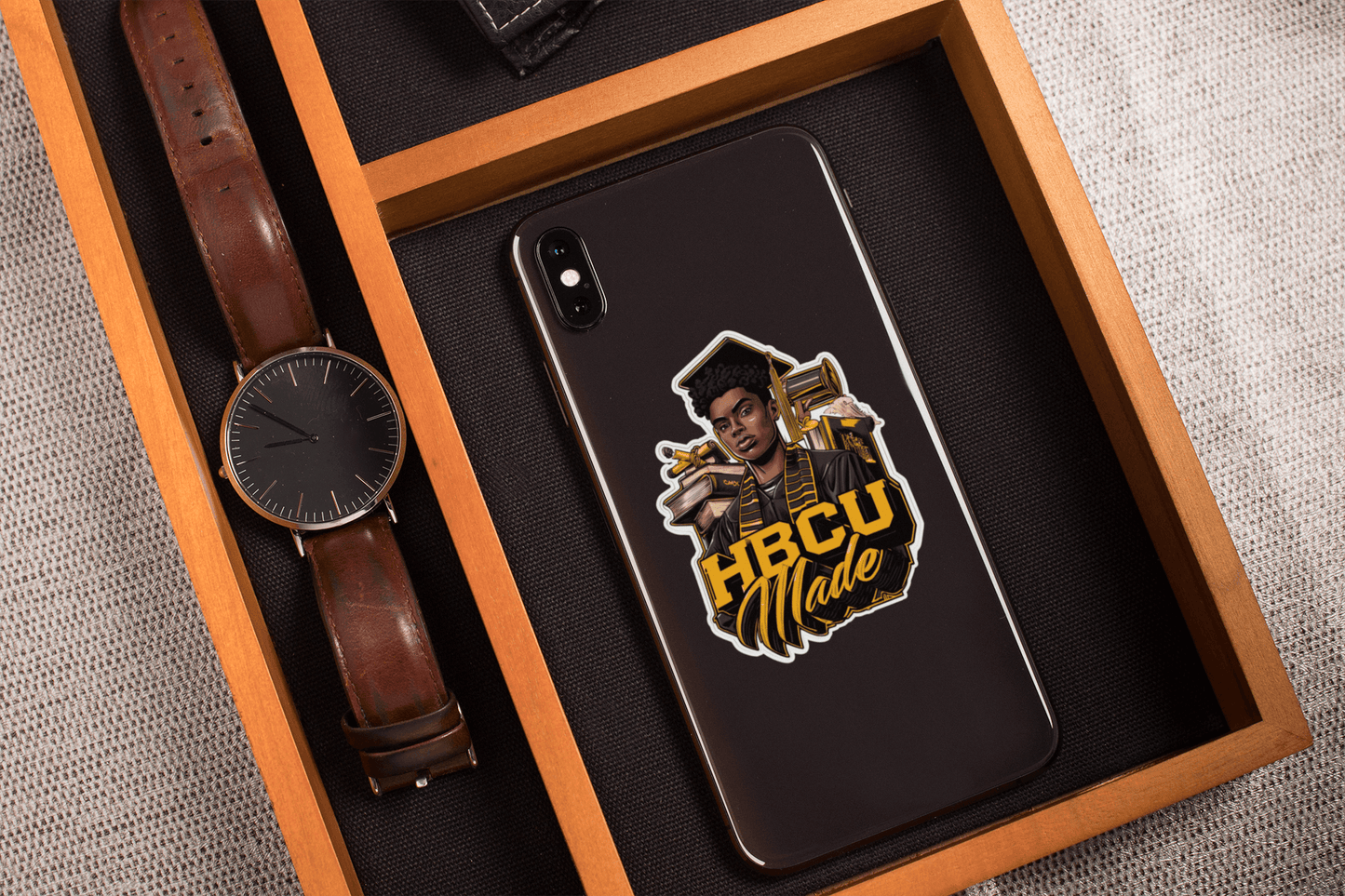 HBCU Made sticker on a phone, showcasing vibrant design and premium vinyl quality in a stylish wooden tray.