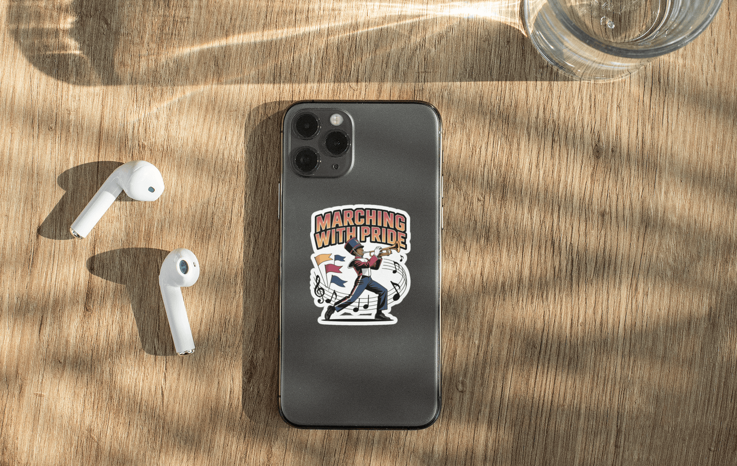 Marching With Pride sticker on a smartphone with earbuds and water glass on a wooden table