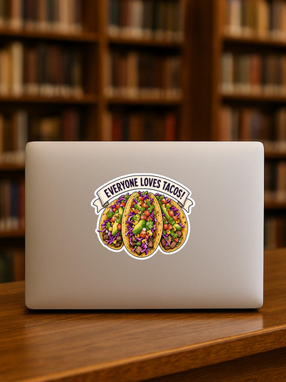 Mockup showing the Everyone Loves Tacos! sticker design on the back of a laptop in front of bookshelves.